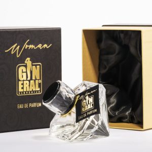 Clear glass perfume bottle with black label and gold text placed in a black-and-gold box set; satin lining visible inside the open box.